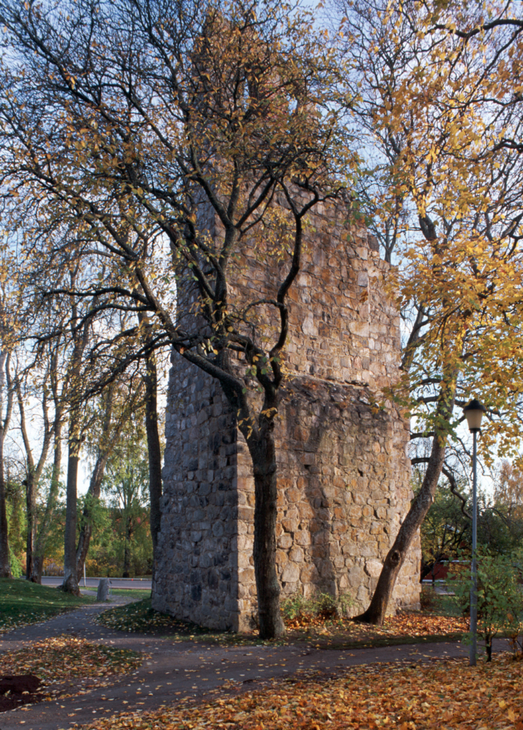 Ruin av stenkyrka delvis skymd av ett träd