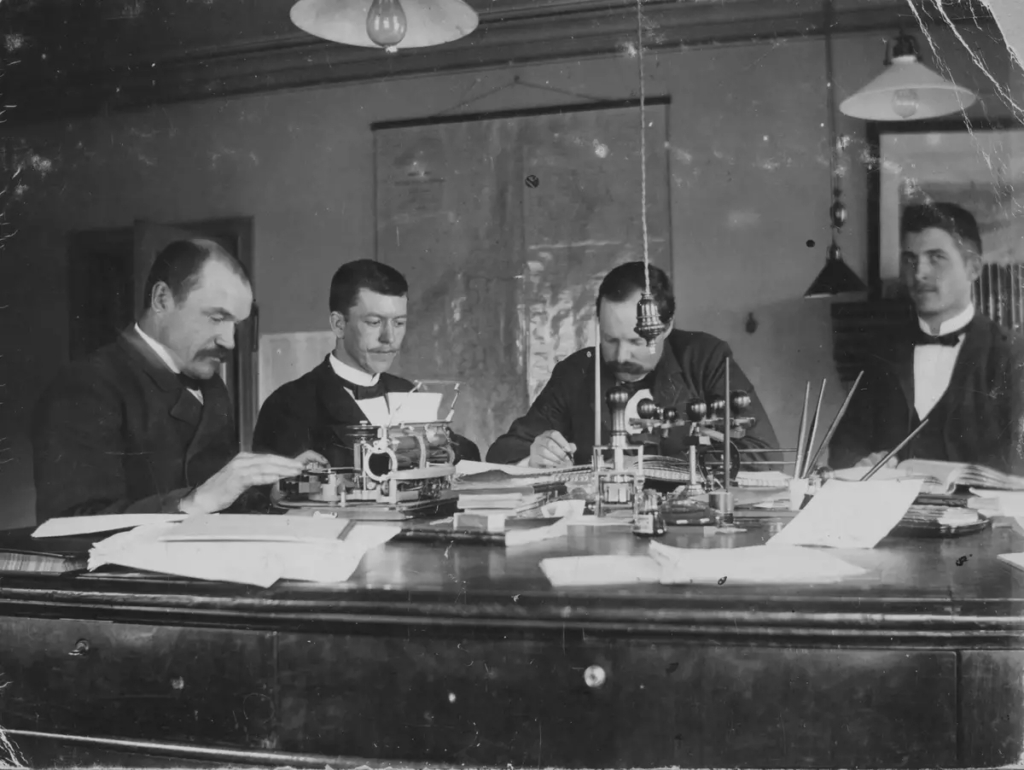 Fyra män sitter runt ett bord och arbetar med att skapa en tidning. Historisk bild.